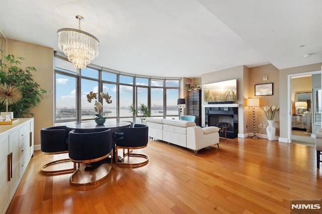 living room with baseboards, a tiled fireplace, an inviting chandelier, a wall of windows, and light wood-type flooring