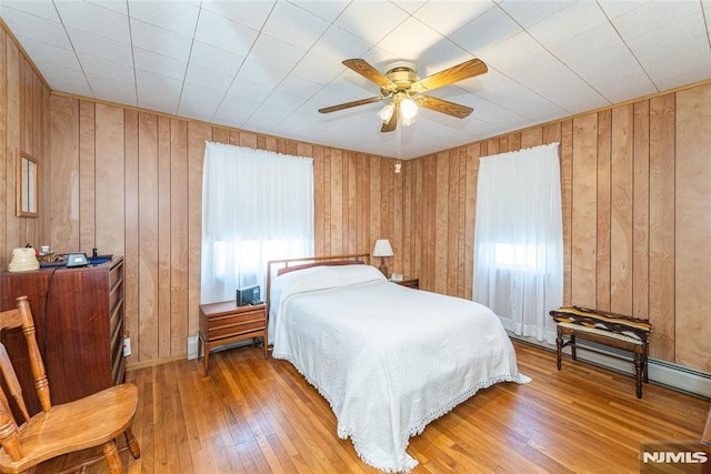 bedroom with ceiling fan, wooden walls, and hardwood / wood-style floors