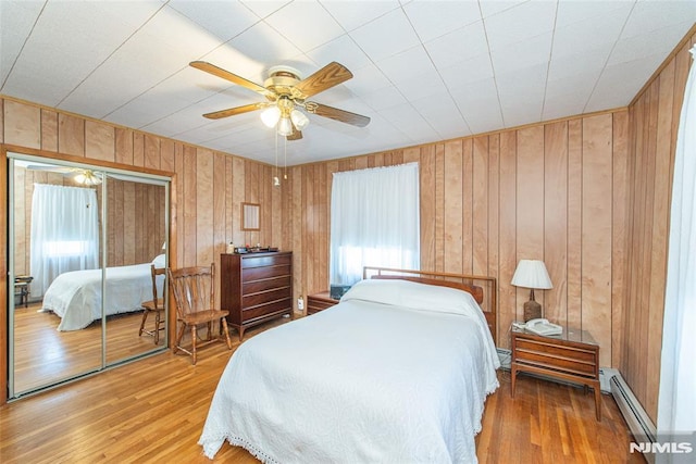 bedroom featuring a baseboard heating unit, wood finished floors, a closet, and a ceiling fan