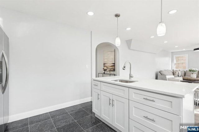 kitchen featuring baseboards, recessed lighting, arched walkways, white cabinetry, and a sink