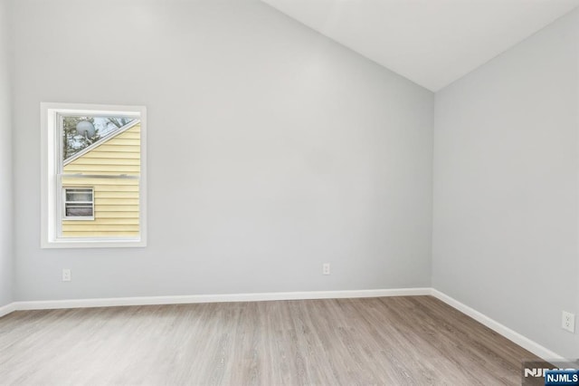 spare room with vaulted ceiling, wood finished floors, and baseboards