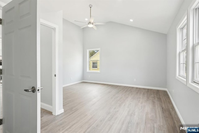 spare room with light wood finished floors, a ceiling fan, baseboards, and vaulted ceiling