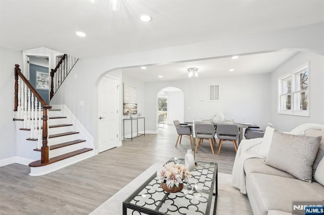 living room featuring visible vents, plenty of natural light, light wood-style floors, and arched walkways