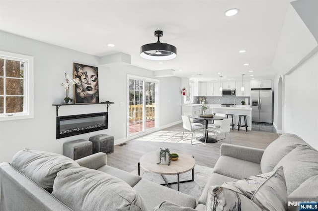 living room featuring a glass covered fireplace, recessed lighting, baseboards, and light wood finished floors