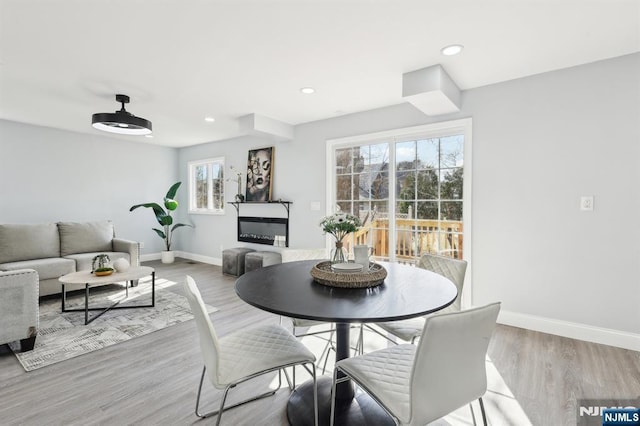 dining area with a glass covered fireplace, recessed lighting, baseboards, and wood finished floors