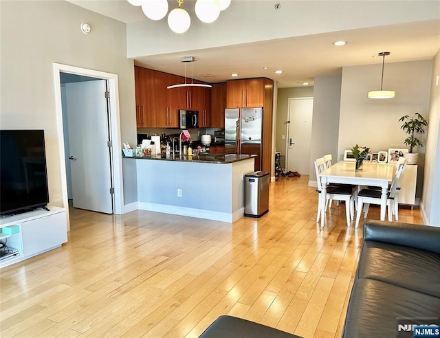 kitchen featuring stainless steel appliances, a peninsula, light wood-style floors, brown cabinetry, and dark countertops