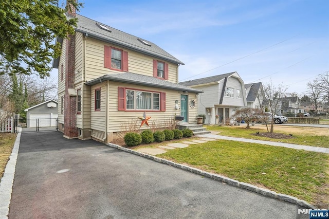 traditional style home with a front yard, fence, a shingled roof, an outdoor structure, and a detached garage