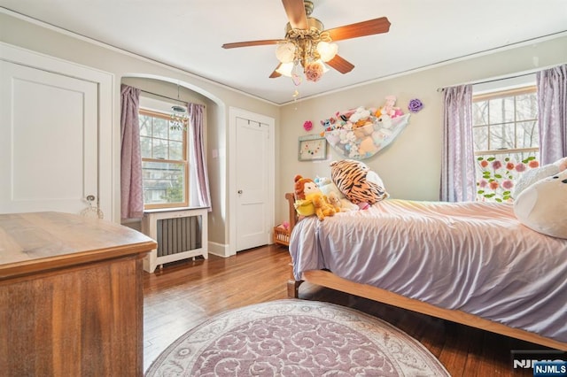 bedroom featuring a ceiling fan, multiple windows, radiator, and wood finished floors