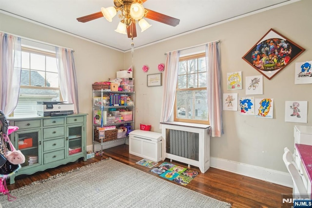 rec room with baseboards, dark wood-type flooring, radiator, and ceiling fan