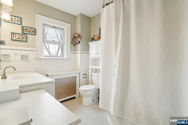 full bathroom featuring a wainscoted wall, toilet, curtained shower, radiator heating unit, and tile walls