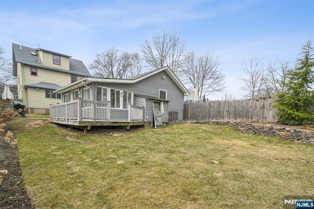 back of house featuring a lawn, a wooden deck, fence, and a sunroom