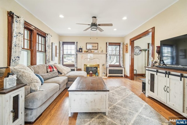 living room featuring a glass covered fireplace, light wood-style flooring, radiator, and ceiling fan