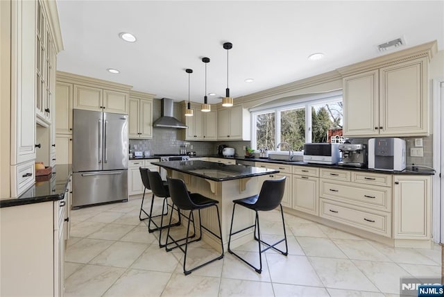 kitchen featuring cream cabinets, high end refrigerator, visible vents, wall chimney exhaust hood, and a kitchen bar