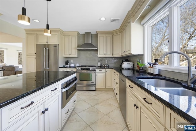 kitchen featuring cream cabinets, a sink, marble finish floor, appliances with stainless steel finishes, and wall chimney range hood