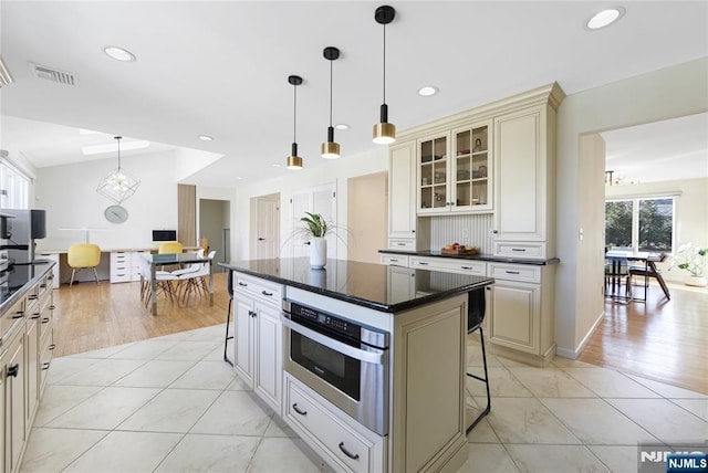 kitchen featuring light tile patterned floors, dark countertops, glass insert cabinets, oven, and cream cabinetry