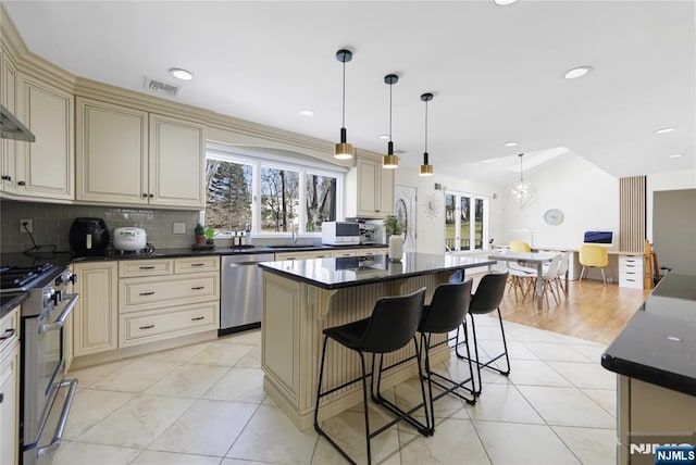 kitchen with appliances with stainless steel finishes, dark countertops, a kitchen island, and cream cabinetry