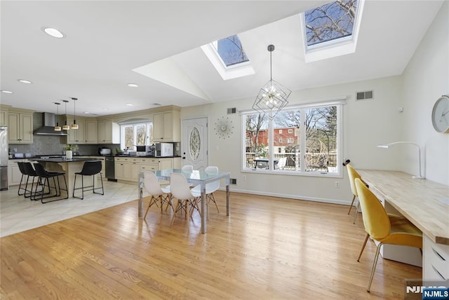 dining space with visible vents, baseboards, lofted ceiling with skylight, light wood-style floors, and a chandelier