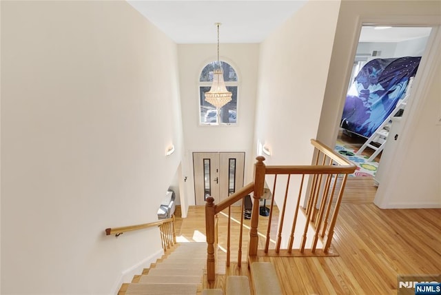 stairs featuring baseboards, wood finished floors, and an inviting chandelier