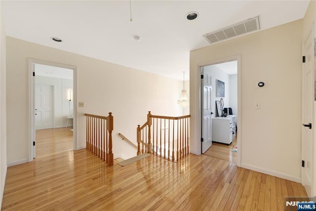 corridor with visible vents, light wood finished floors, an upstairs landing, and baseboards