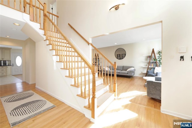 stairway with recessed lighting, wood finished floors, a towering ceiling, and baseboards