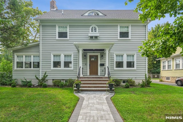 view of front facade featuring roof with shingles, a front lawn, and a chimney