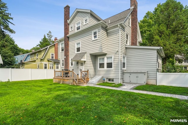 back of property with a fenced backyard, a chimney, a wooden deck, and a yard