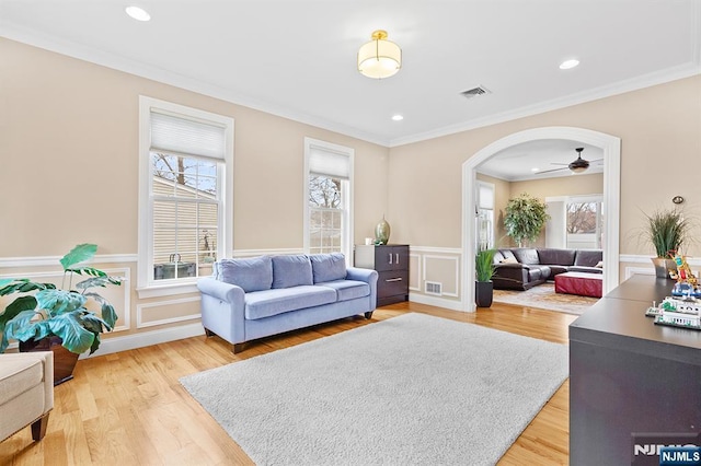 living area featuring arched walkways, visible vents, light wood finished floors, and wainscoting