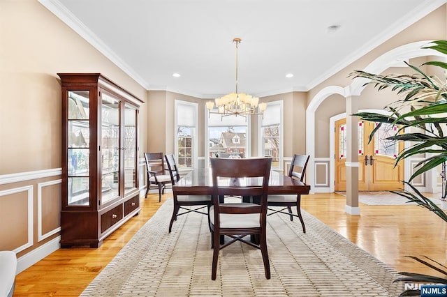 dining area with a wainscoted wall, an inviting chandelier, light wood-style flooring, ornamental molding, and a decorative wall