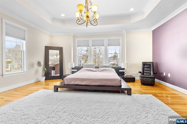 bedroom with wood finished floors, baseboards, a tray ceiling, ornamental molding, and a notable chandelier