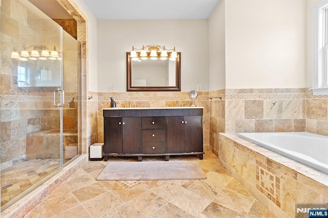 full bathroom featuring a wainscoted wall, double vanity, a shower stall, a garden tub, and tile walls