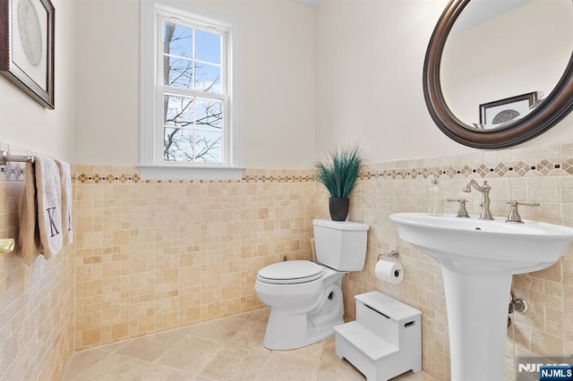 bathroom with a wainscoted wall, toilet, tile walls, and tile patterned flooring