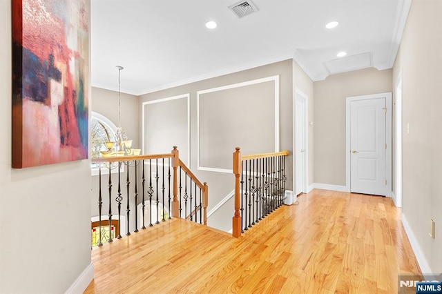 corridor featuring wood finished floors, baseboards, visible vents, ornamental molding, and an upstairs landing