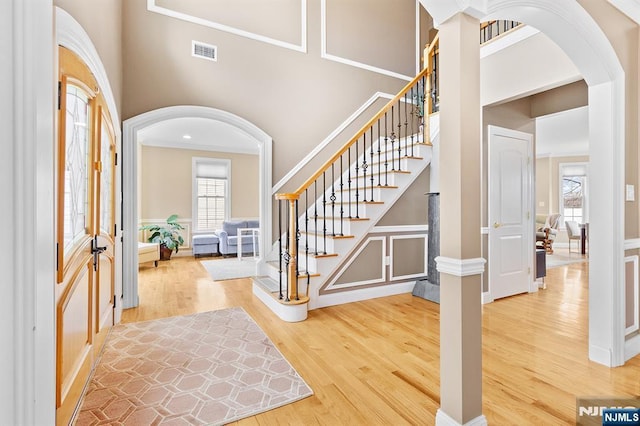 entryway with wood finished floors, visible vents, arched walkways, and a towering ceiling