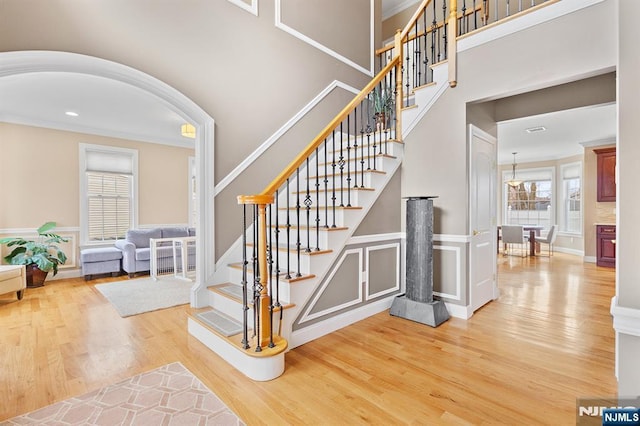 stairs featuring ornamental molding, wainscoting, a towering ceiling, wood finished floors, and arched walkways