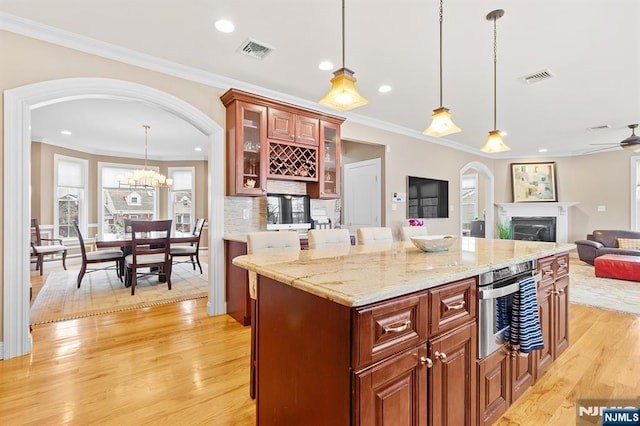 kitchen with arched walkways, a fireplace, visible vents, and light wood-type flooring