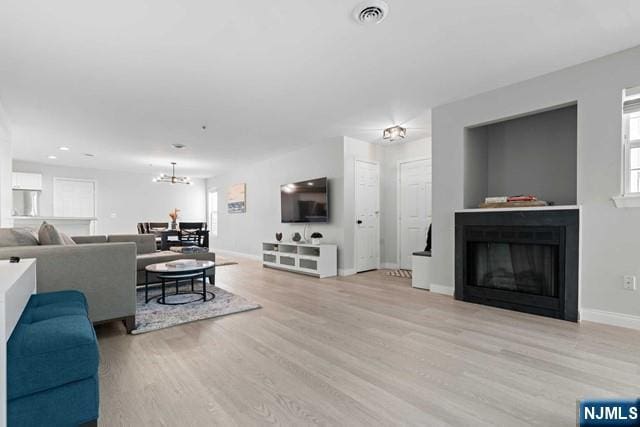 living room featuring a fireplace, visible vents, light wood-style flooring, a chandelier, and baseboards