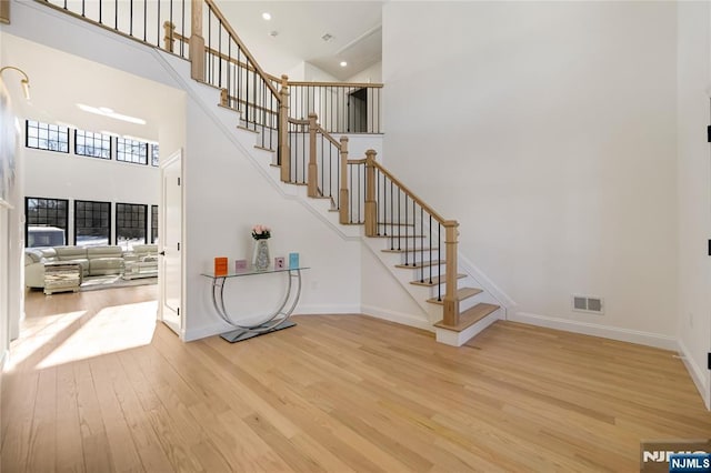 stairway featuring a high ceiling, wood finished floors, visible vents, and baseboards