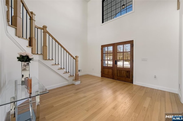 entrance foyer featuring french doors, stairway, a high ceiling, light wood-style floors, and baseboards