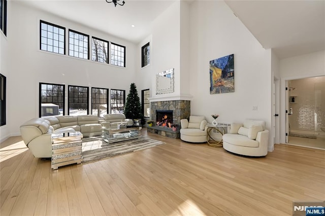 living area with a stone fireplace, a towering ceiling, and wood finished floors