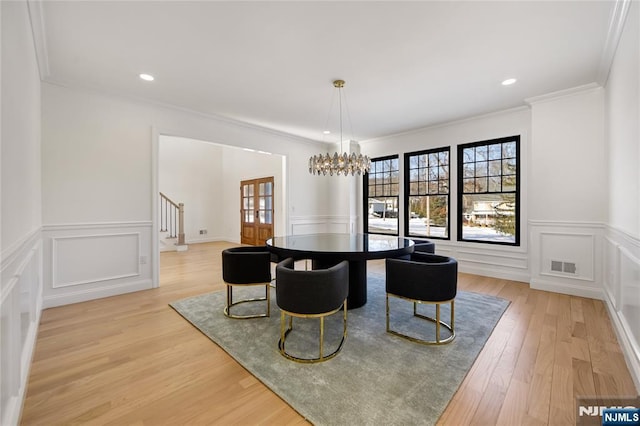 dining area featuring light wood-style flooring, a decorative wall, visible vents, stairway, and an inviting chandelier