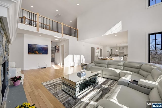 living area with recessed lighting, a fireplace, wood finished floors, a towering ceiling, and visible vents