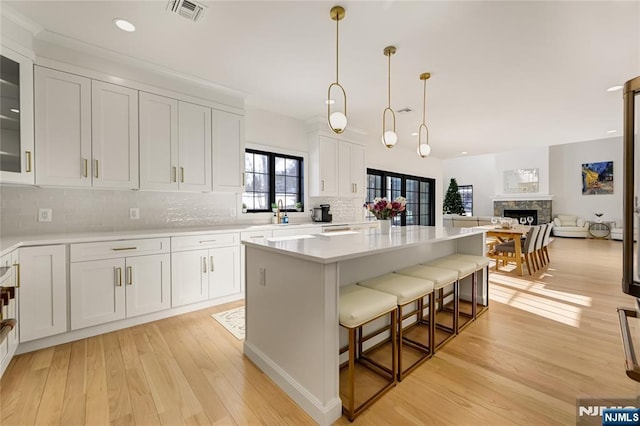 kitchen with visible vents, decorative backsplash, white cabinets, light wood-style flooring, and light countertops