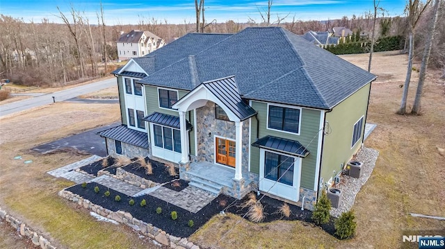 view of front of property featuring stone siding, cooling unit, a standing seam roof, and metal roof