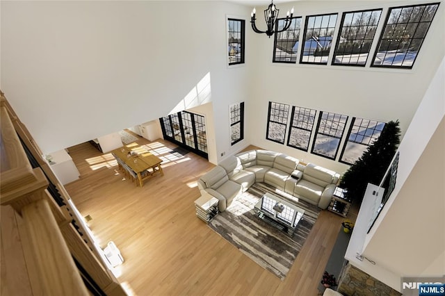 living room with an inviting chandelier, plenty of natural light, a high ceiling, and wood finished floors