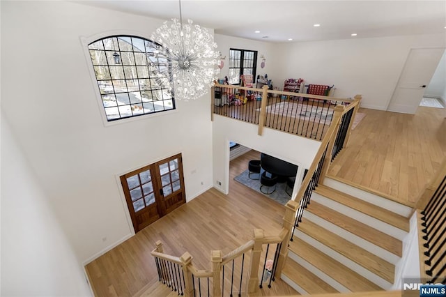 stairway with french doors, recessed lighting, wood finished floors, and a notable chandelier