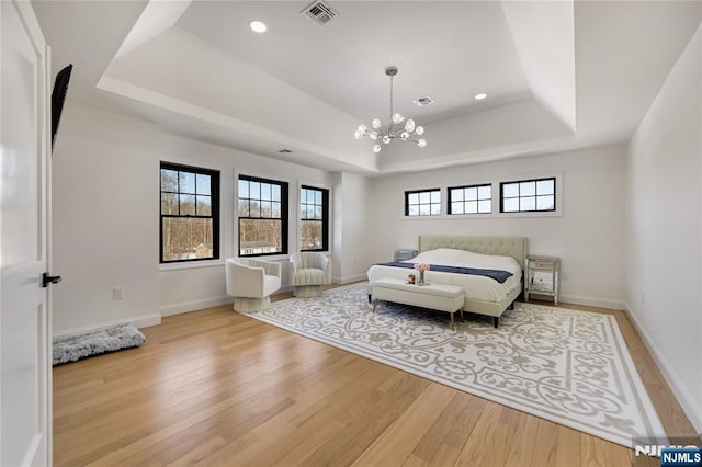 bedroom with light wood finished floors, a raised ceiling, visible vents, and baseboards