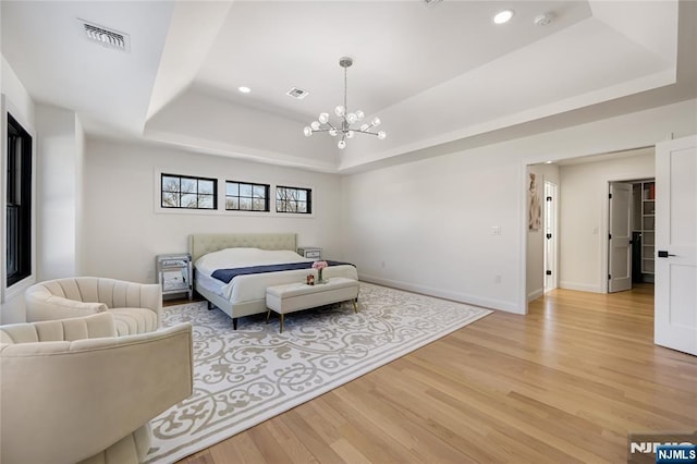 bedroom featuring a raised ceiling, visible vents, a notable chandelier, and light wood-style flooring