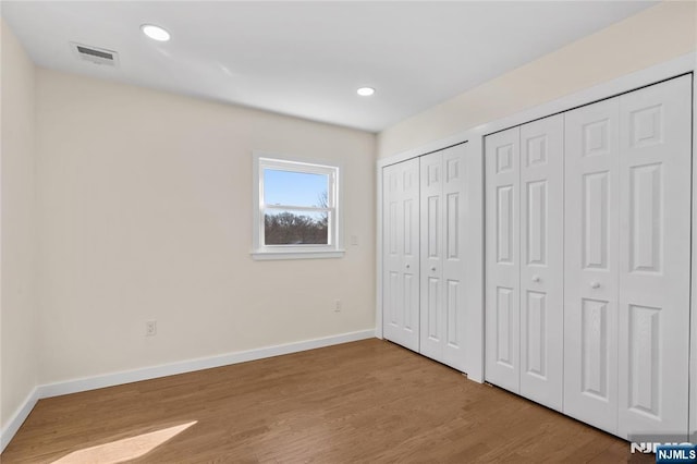 unfurnished bedroom with baseboards, visible vents, wood finished floors, two closets, and recessed lighting