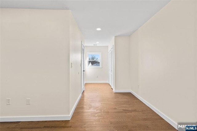 hallway featuring baseboards, wood finished floors, and recessed lighting