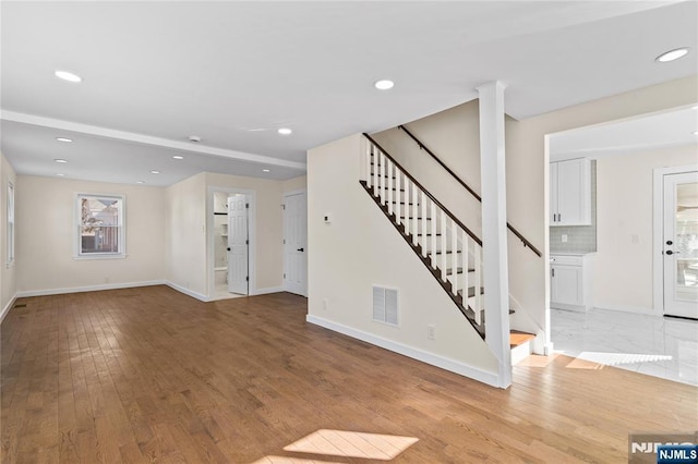 unfurnished living room with light wood-type flooring, stairway, baseboards, and recessed lighting